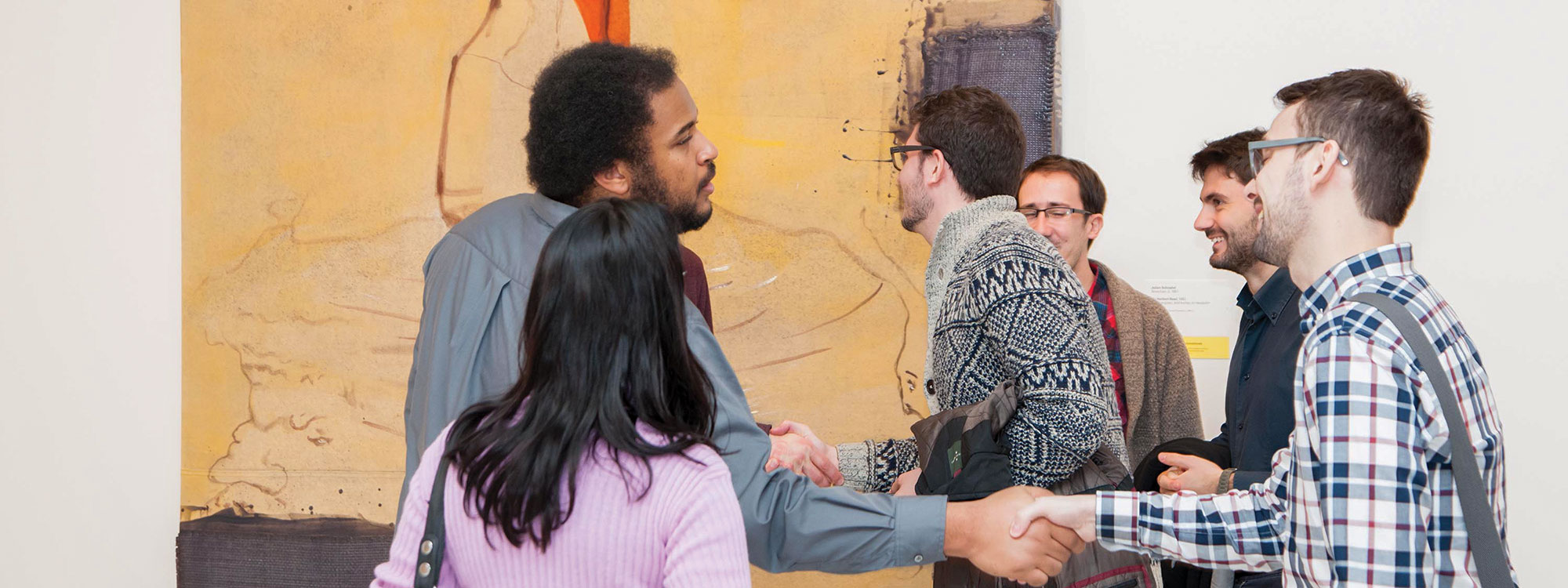 A group of museum-goers greeting each other in front of a large painting in the gallery.