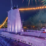 A dramatic photo of a submarine at night with lights and fireworks around it.