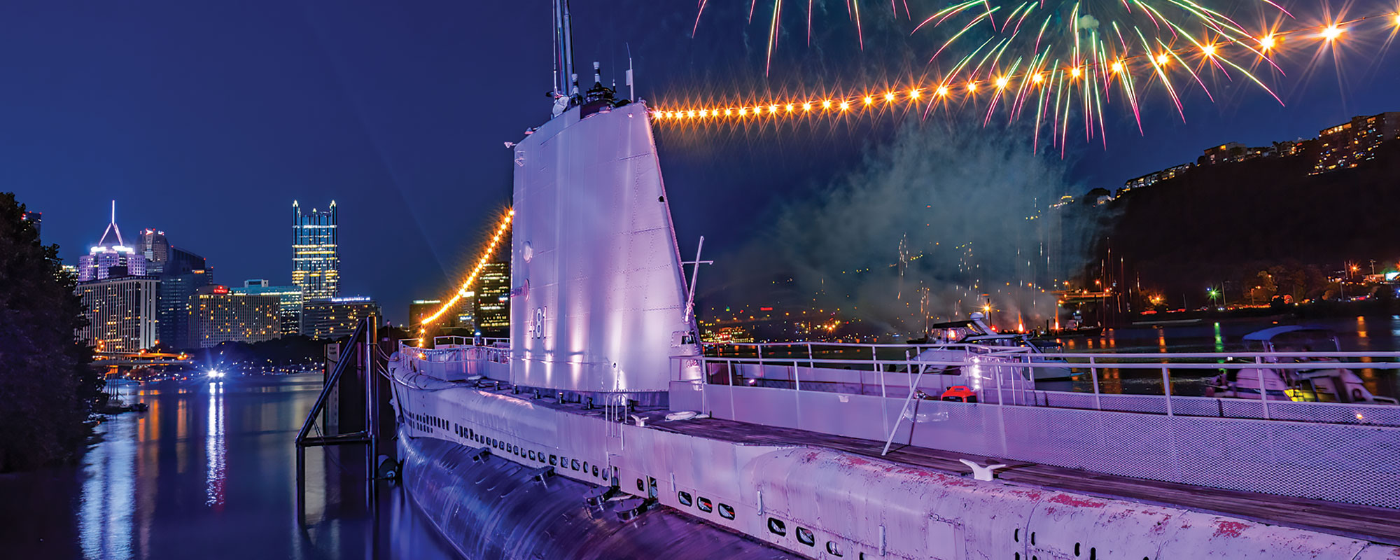 A dramatic photo of a submarine at night with lights and fireworks around it.