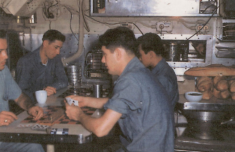 a vintage photo of the crew of a submarine playing cards in the mess hall area.