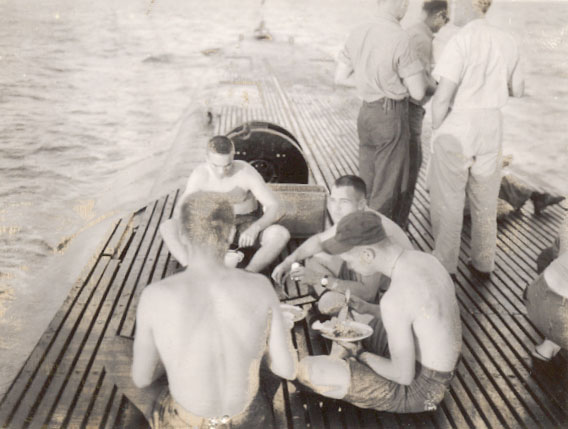 a vintage photo fo crew members of a submarine eating on the deck.