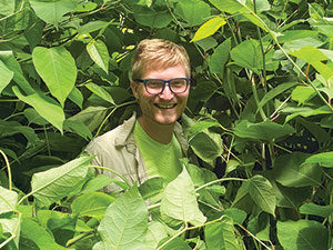 man surrounded by green plants with only his face visible.