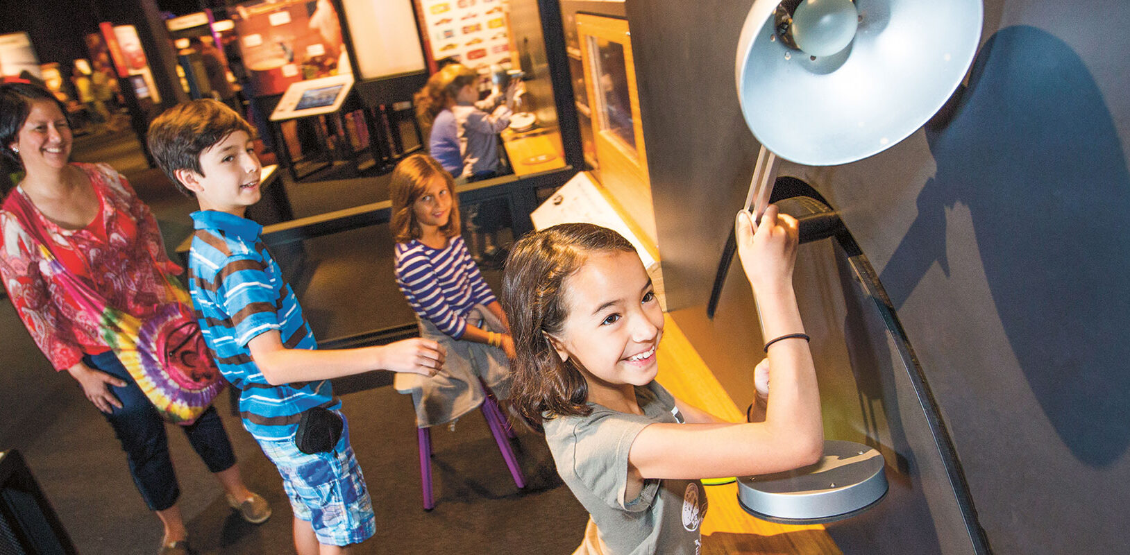 A group of children exploring an exhibit of a lamp.