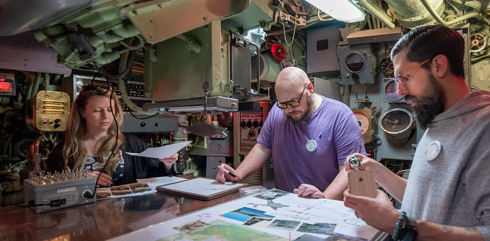 Three people working together at a table inside of a submarine.