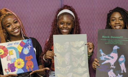 Three smiling individuals hold colorful art pieces against a purple backdrop. The art includes vibrant flowers, butterflies, and pigeons. Energetic and creative atmosphere.