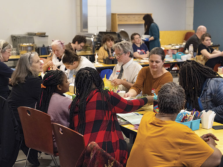 A group of diverse people of various ages gather around tables, engaging in arts and crafts. The atmosphere is collaborative and lively.