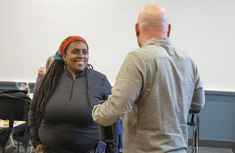 A person with long braids in a black shirt listens intently to a man in a light-colored shirt during a meeting or discussion.