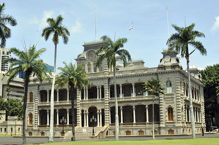 Historic palace with ornate architecture, arches, and columns, surrounded by tall palm trees under a clear blue sky. Elegant and serene atmosphere.