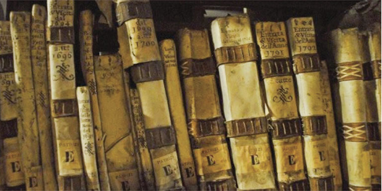 A row of aged, leather-bound books with faded, handwritten titles and ornate designs on their spines. The scene conveys a sense of history and antiquity.