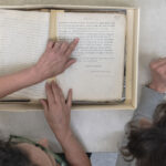 Two people examine an open archival box with historical documents, pointing and discussing the contents together.