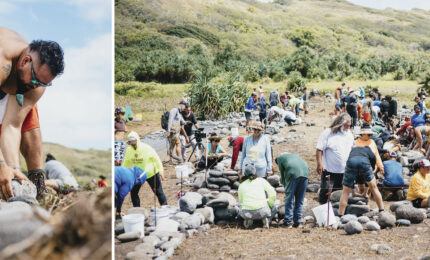 A group of people work together outdoors, carefully arranging stones on the ground under a sunny sky, amidst lush greenery.