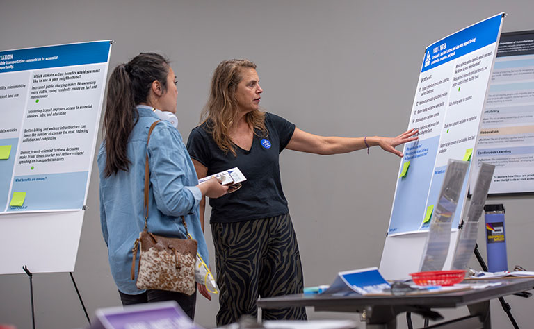 Staff member explains an educational poster to a visitor at an information booth, creating an engaged, welcoming atmosphere.