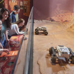 Museum visitors explore an interactive Mars exhibit, viewing robotic rovers on a red, rocky landscape through glass; curious mood.