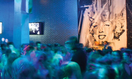 A blurred image of a group of teens dancing in the Andy Warhol Museum lobby.