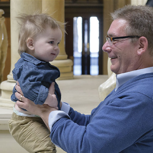 A man holds a young child in a casual setting, surrounded by elegant columns and soft lighting.