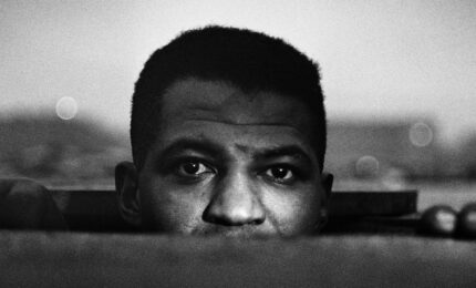 Close up of a man's head and hands as he peeks out of an manhole, taken at street level.