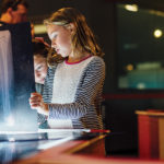 Two young girls looking at x-rays of human bones on a light table..