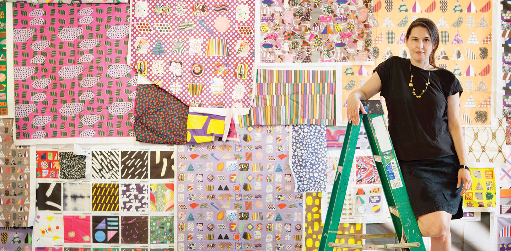 ARtist Ruth Root standing on a ladder in front of digitally printed fabric swatches.