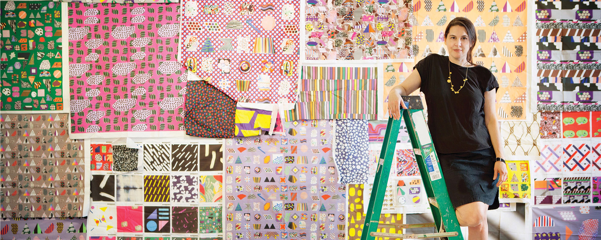 ARtist Ruth Root standing on a ladder in front of digitally printed fabric swatches.