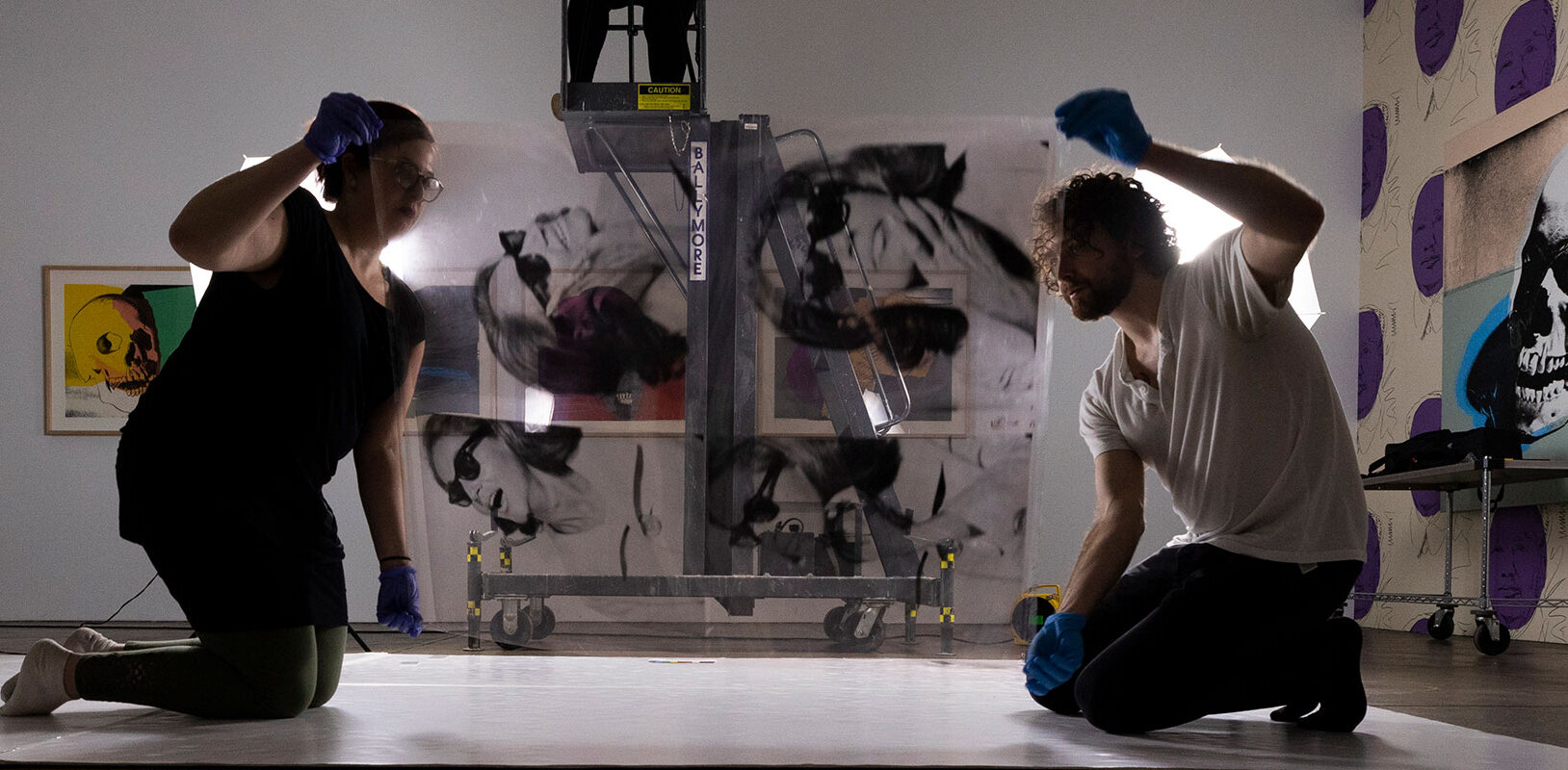 Art preparators handle an acetate depicting art collector Ethel Scull. Digital collections assistant is elevated on a cherry picker, to photograph an acetate.