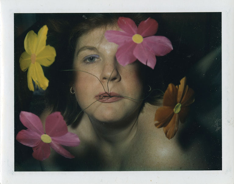A polaroid od Bridget Berlin with fake flowers being held in her mouth