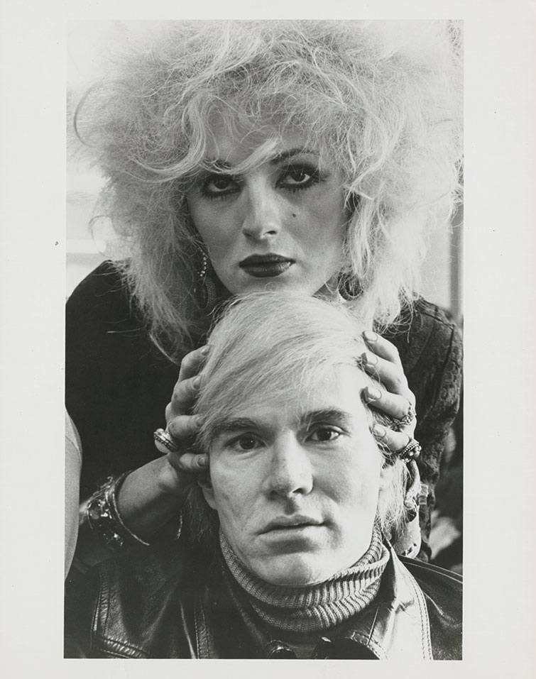 A photo of Candy Darling standing behind Andy Warhol, with her hands holding his head