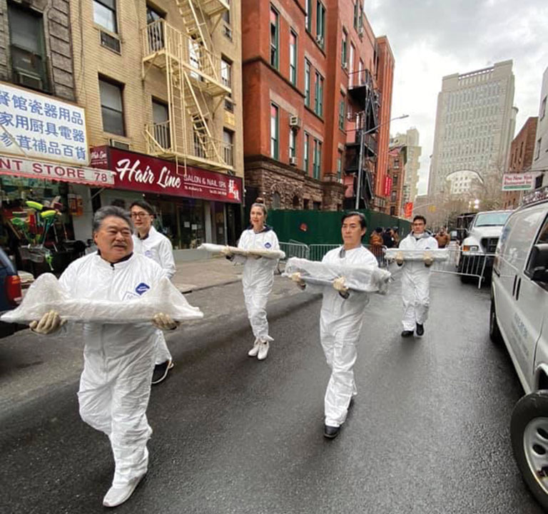 People in hazmat suits carrying objects on a street