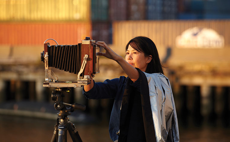 A colorful photo of a women standing next to a large camera