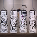 A row of 10 punching bags hanging in a gallery painted with depictions of Jesus