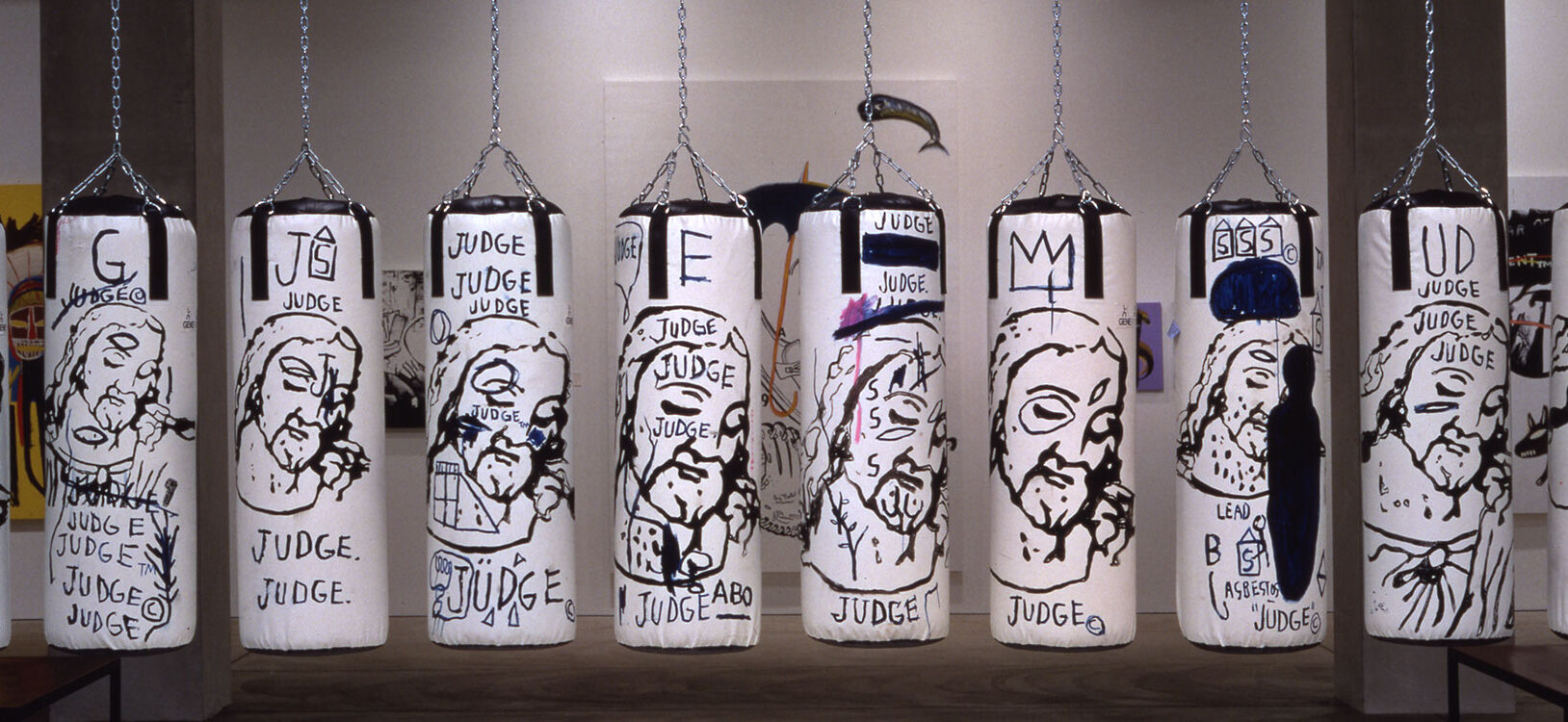 A row of 10 punching bags hanging in a gallery painted with depictions of Jesus
