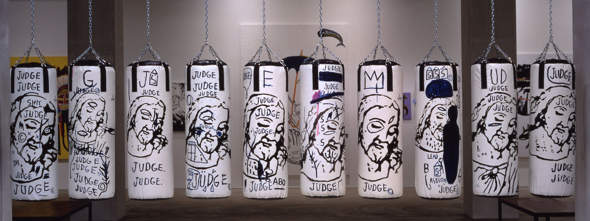A row of 10 punching bags hanging in a gallery painted with depictions of Jesus