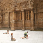 Young children drawing on the floor in front of a large structure in the hall of architecture