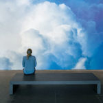 A woman sitting in front of a large photo of clouds
