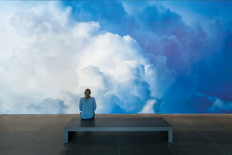A woman sitting in front of a large photo of clouds
