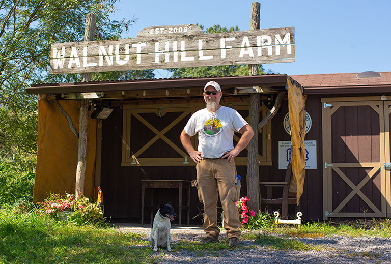 A man standing in front of a building with a sigh saying Walnut Hill Farm