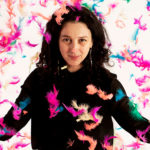 Artist Paola Pivi standing with feathers falling around her