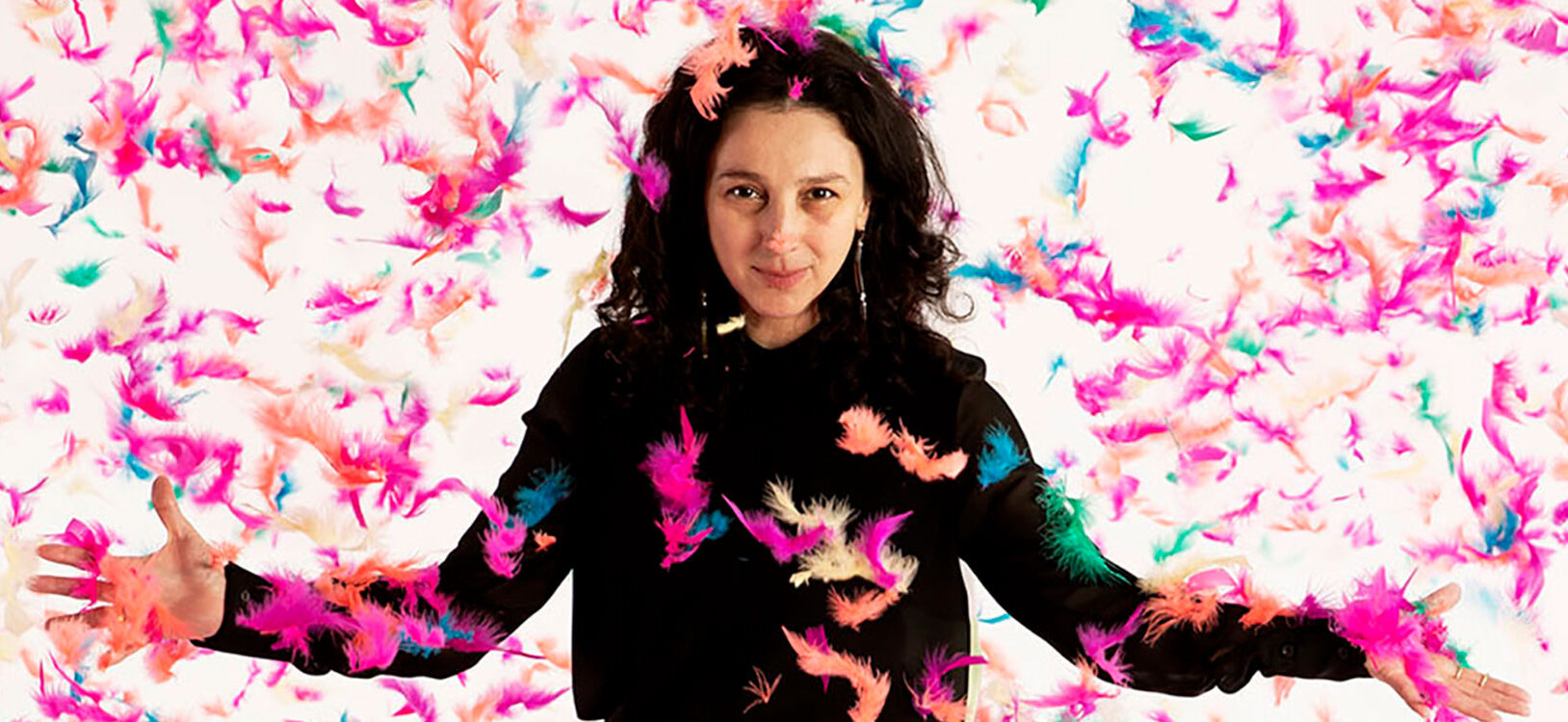 Artist Paola Pivi standing with feathers falling around her