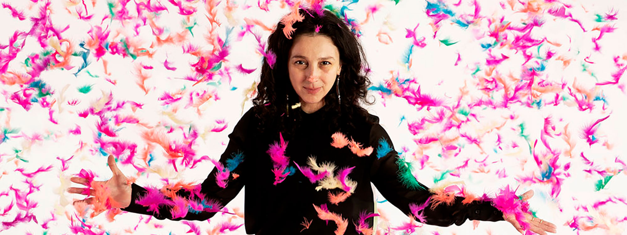 Artist Paola Pivi standing with feathers falling around her