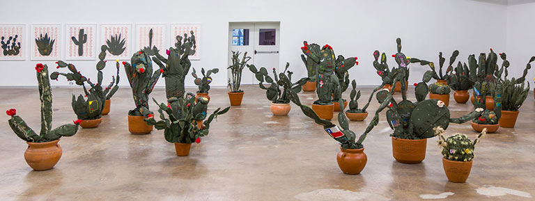 An installation view of room full of cacti made from uniforms of border patrol officers