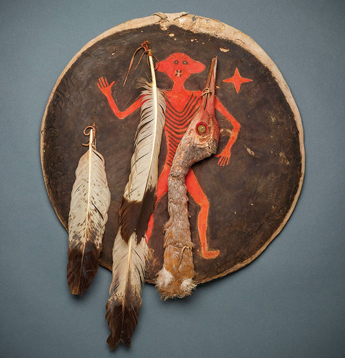 a brown war shield with feathers attached with a primitive drawing of a man