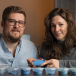 Two scientists posing with a blue powder in a petri dish