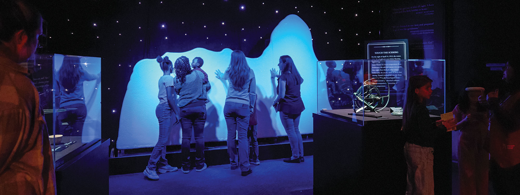 Museum goers touching a large exhibit of an iceberg.