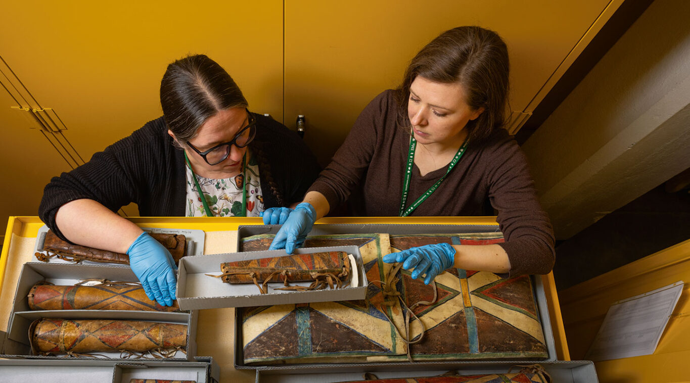 Two female curators examine a draw of native american artifacts.
