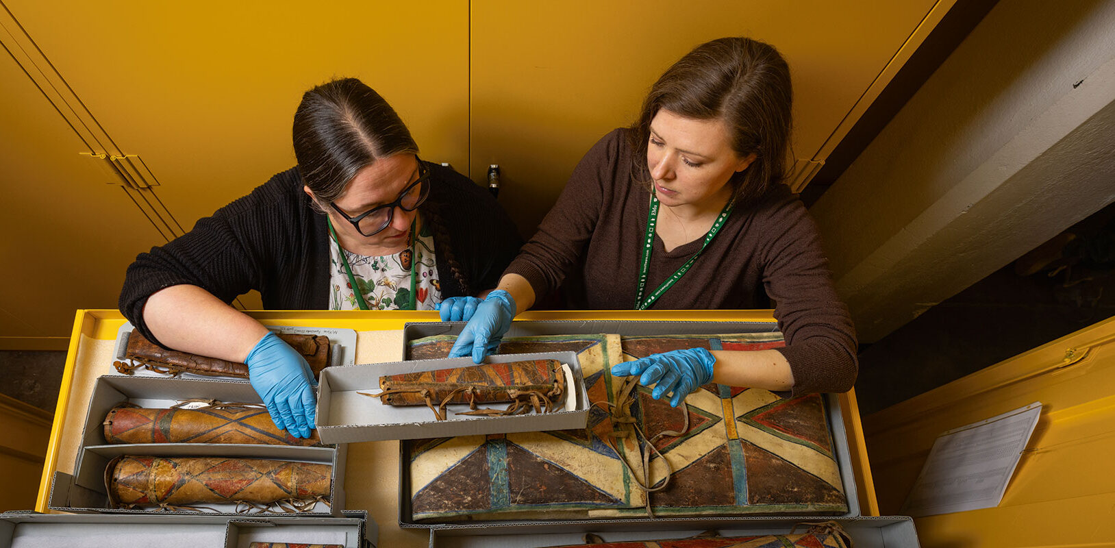 Two female curators examine a draw of native american artifacts.
