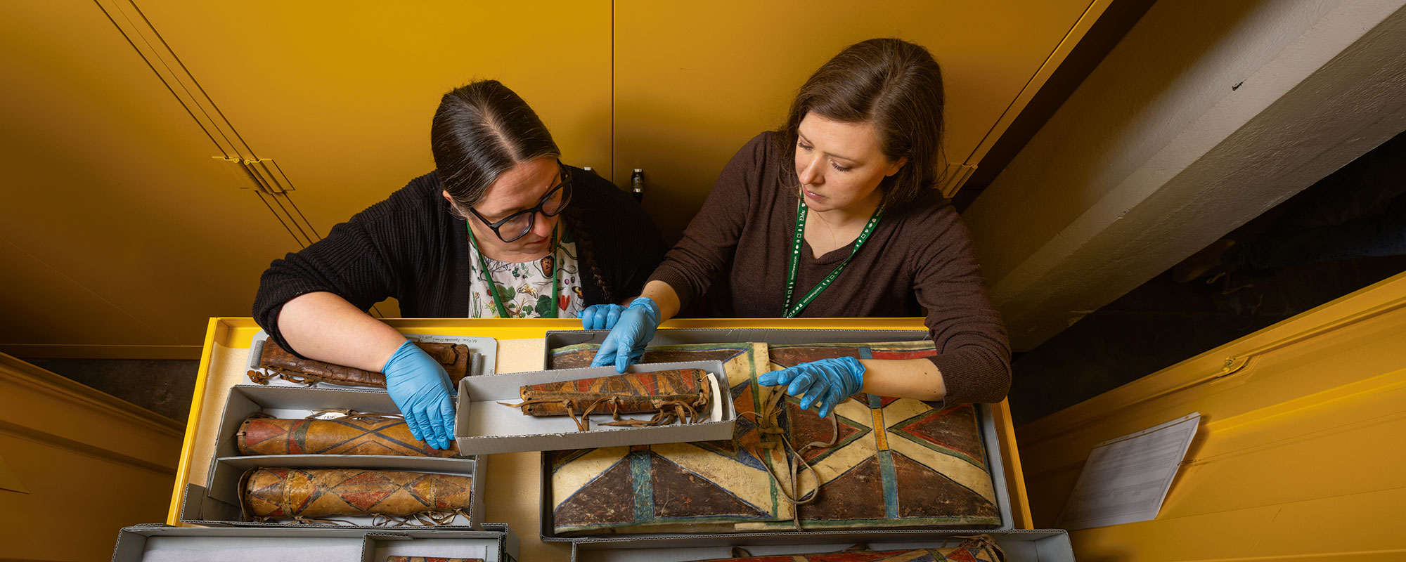 Two female curators examine a draw of native american artifacts.