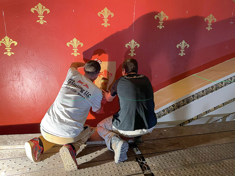 Two workers stenciling fleur de lis on the wall of the music hall.