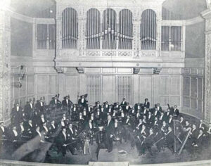 A vintage black and white photo of the Pittsburgh Symphony in the Carnegie Music Hall.