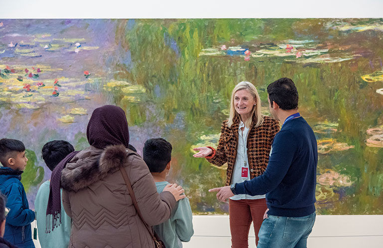 An art museum educator leading a tour of the museum with monet's water lillies in the background.