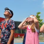 A group of children staring at the solar eclipse wearing protective glasses.