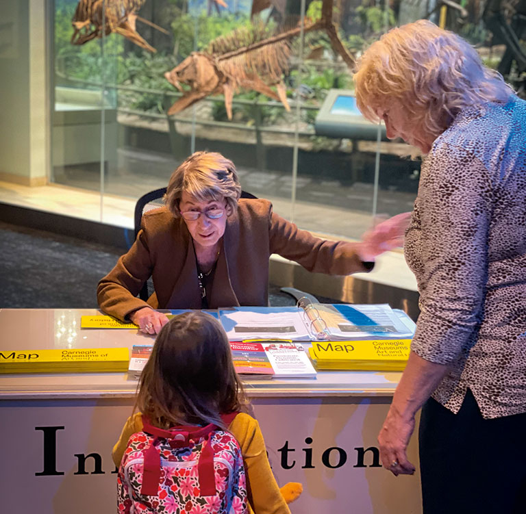 a senior aged woman at an information desk talking to a young girl and her mother.